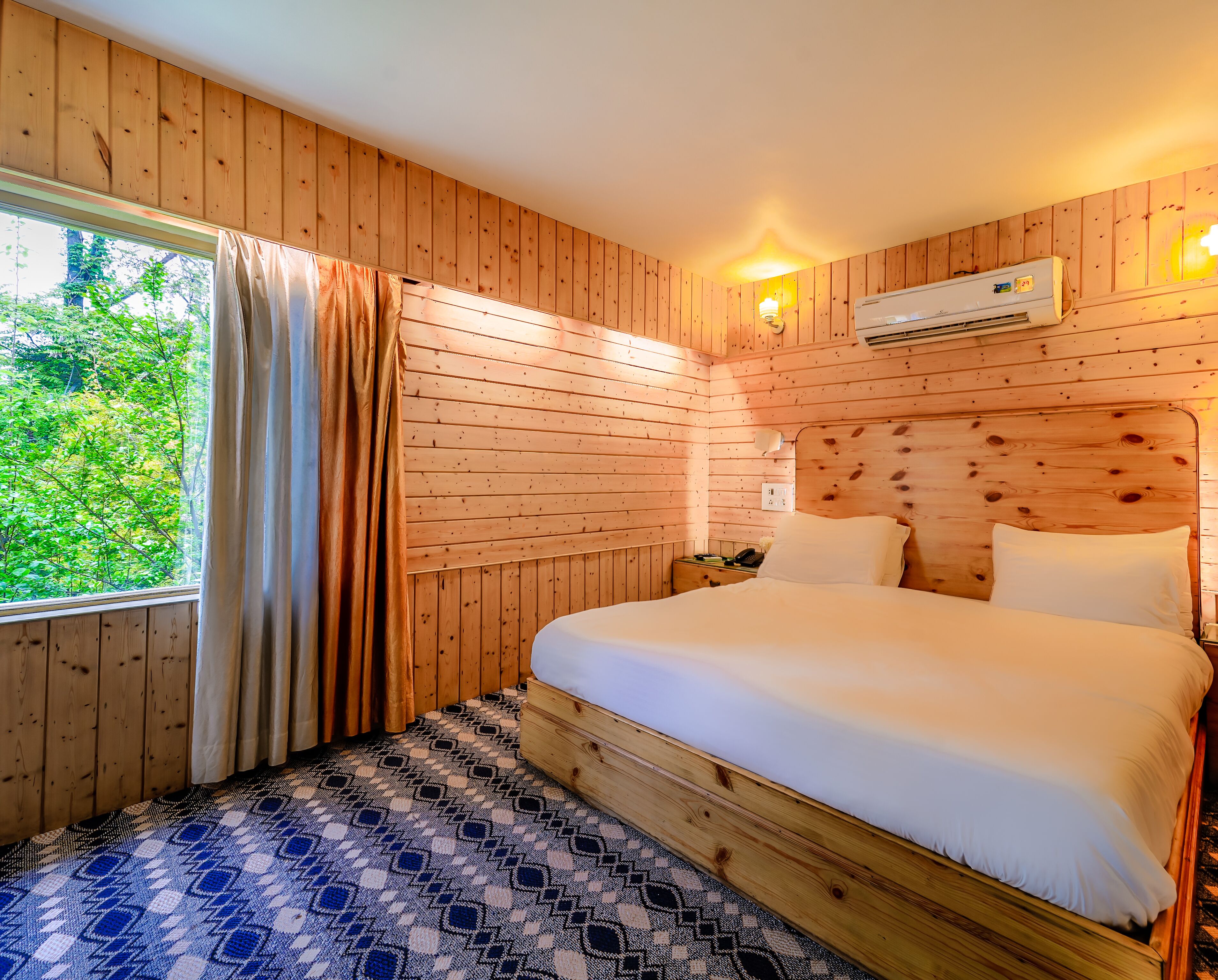 A wooden-paneled room with a bed, a window with curtains, and an air conditioning unit.