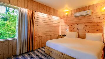 A wooden-paneled room with a bed, a window with curtains, and an air conditioning unit.
