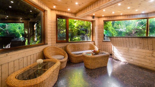 A wooden interior with wicker furniture, large windows, and a glass table. - Hotel Mirage (Srinagar)