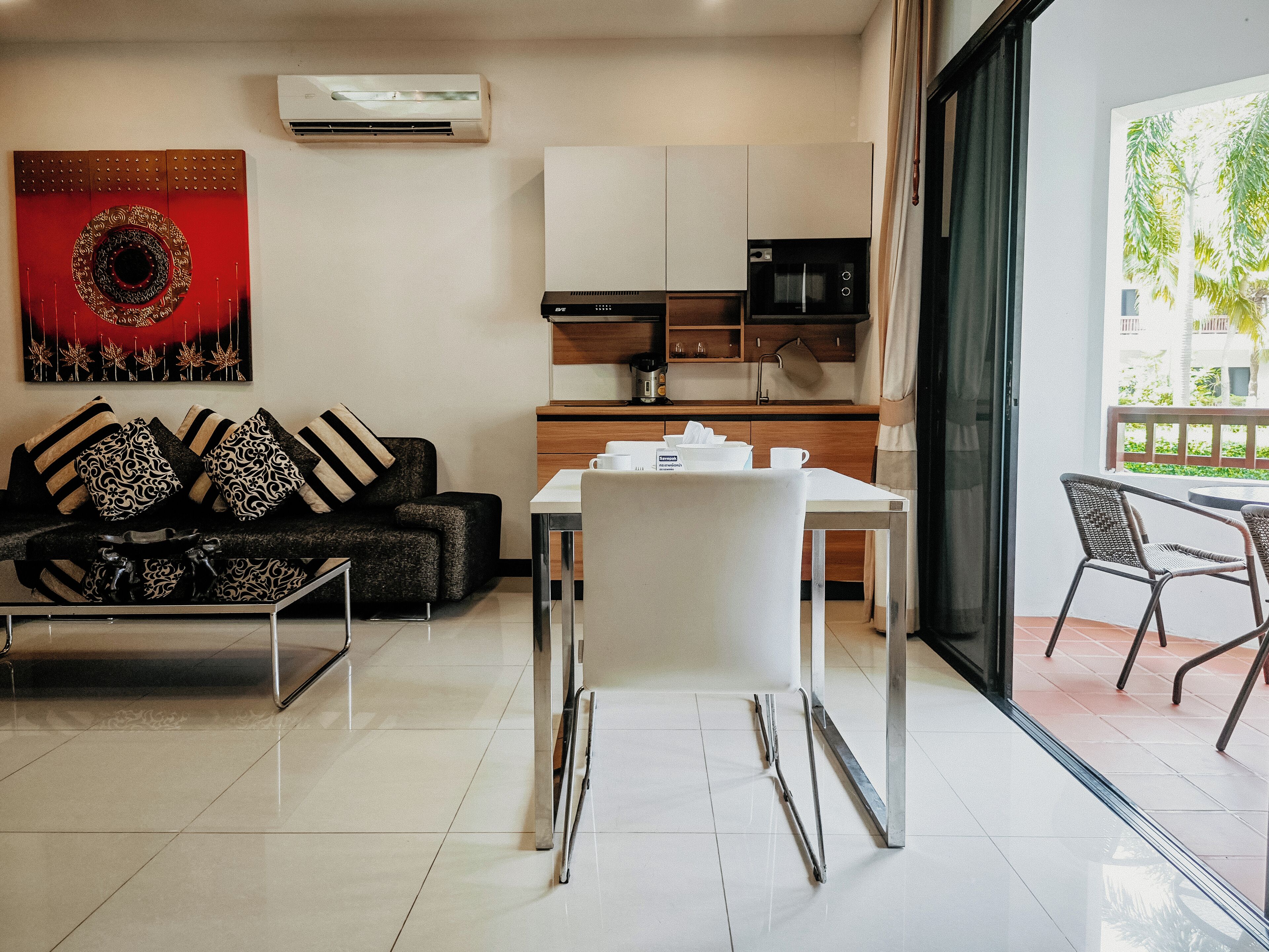 Un salon moderne avec un canapé, une table à manger et des chaises. Il y a un coin cuisine équipé d’un four à micro-ondes et d’un évier. La pièce est dotée d’une grande fenêtre offrant une vue sur la verdure environnante.