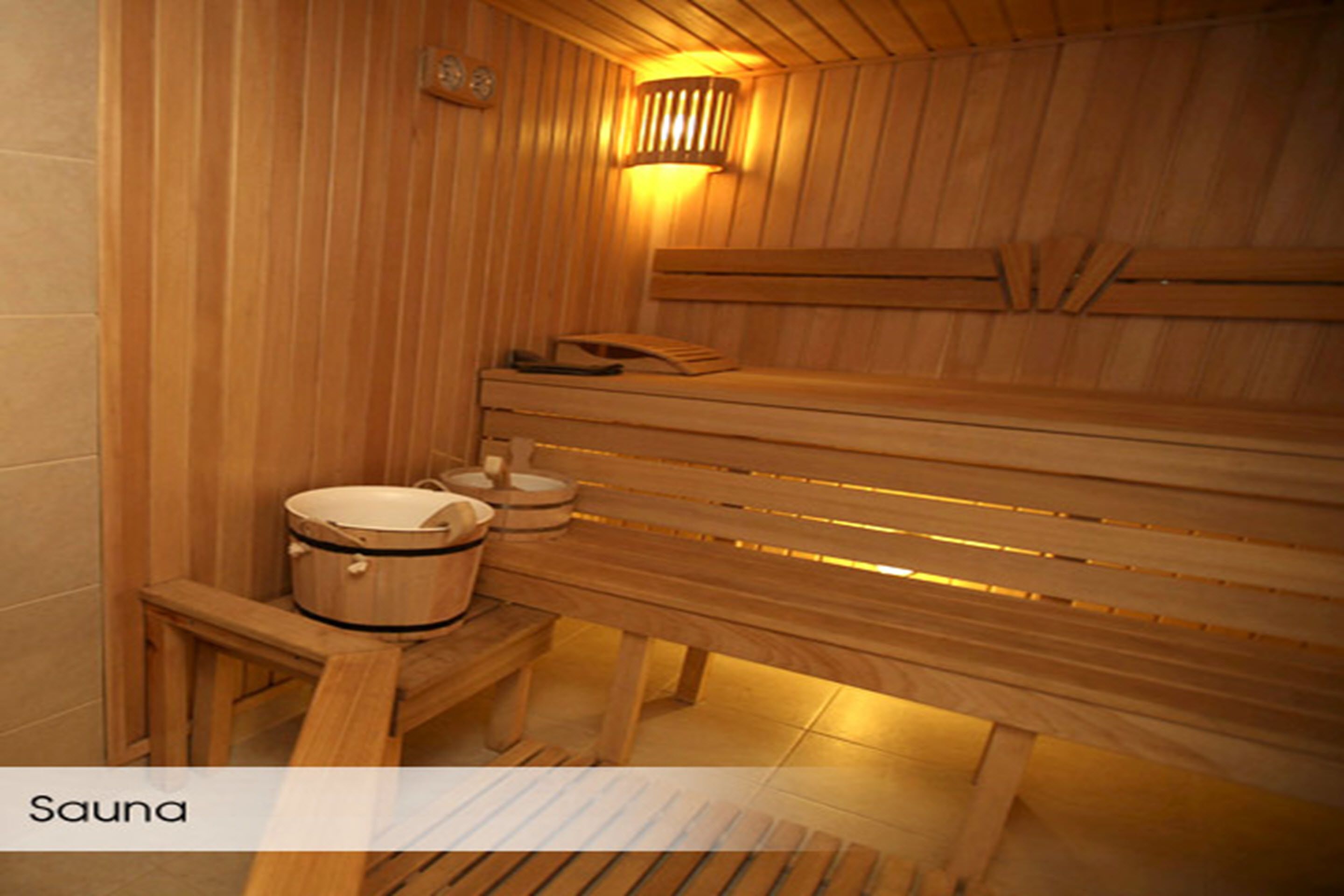 A sauna with wooden benches, a bench heater, and a wooden table with a pot and a bucket.