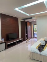 Quarto de hotel moderno com televisão de tela plana, parede revestida de madeira, guarda-roupa espaçoso, cama com cabeceira decorativa e vista para o exterior.