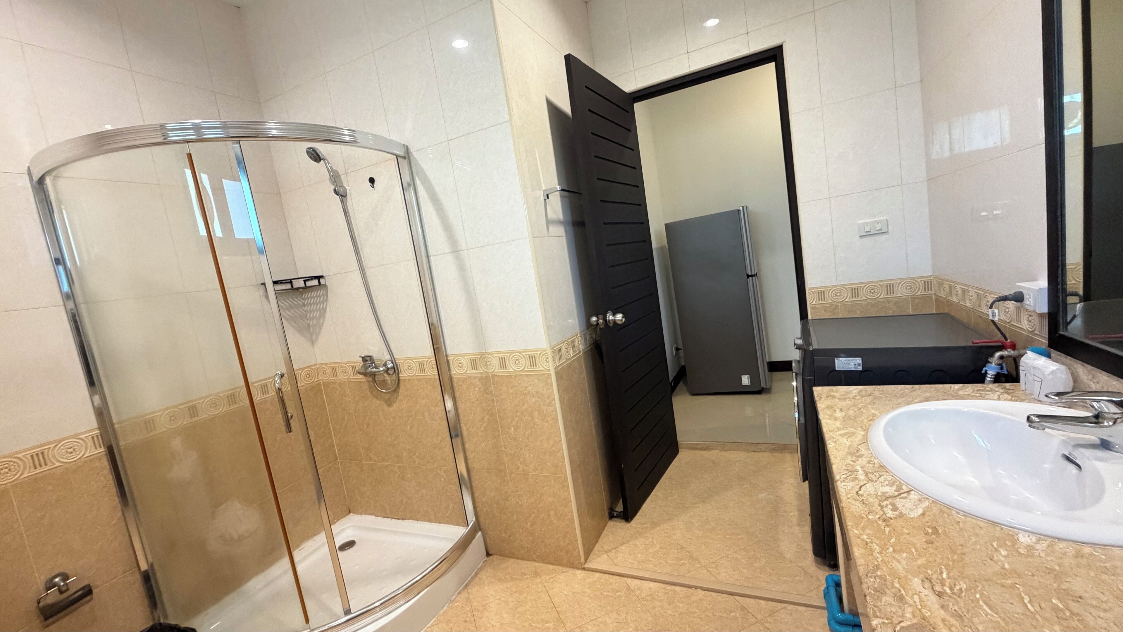Un baño con ducha envuelta en vidrio, un lavamanos con espejo y una puerta que da a otra habitación.