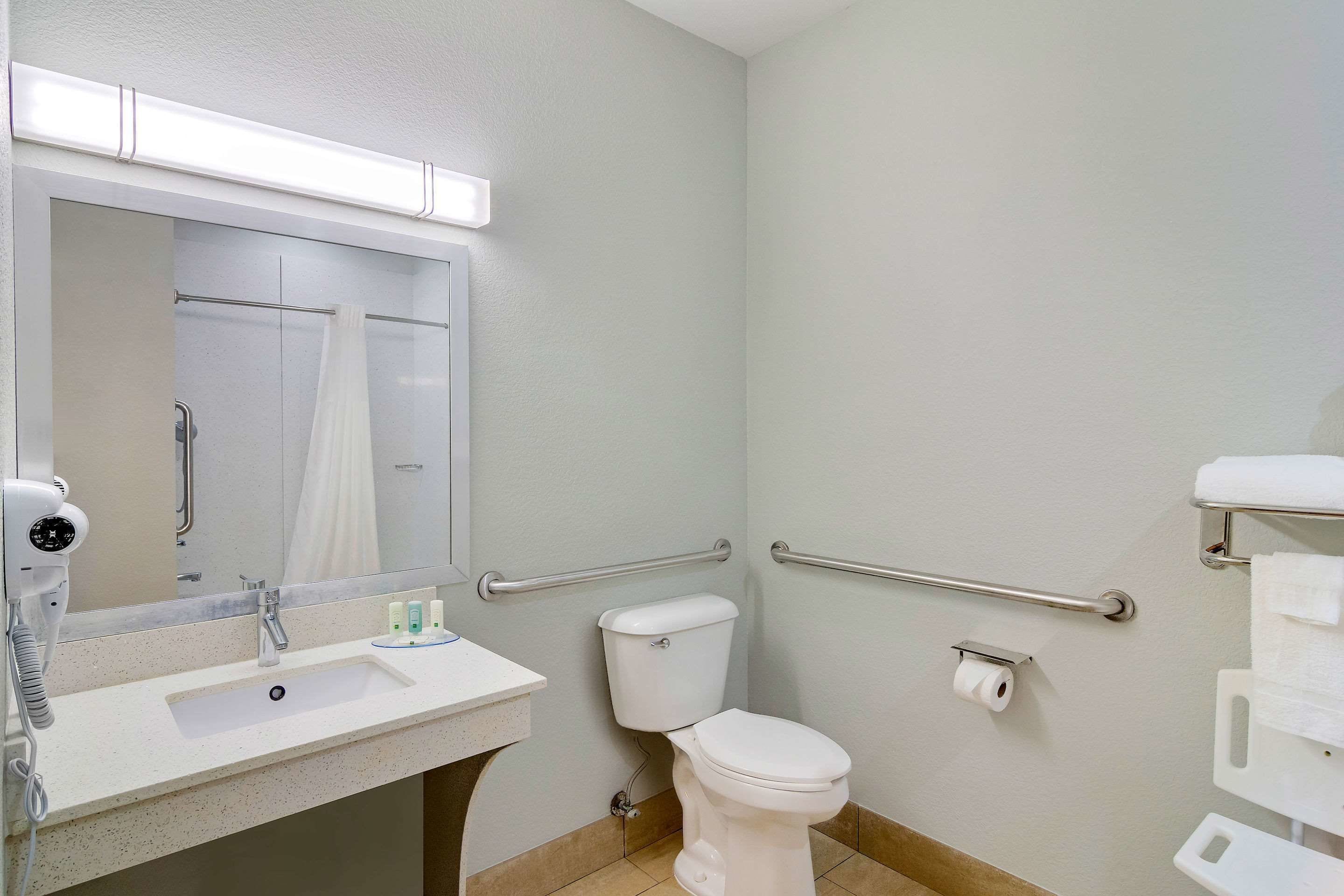 Une salle de bain équipée d’un lavabo, d’un miroir, de toilettes et de barres d’appui.