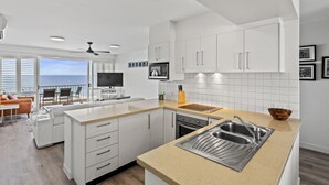 Ett modernt kök med vita skåp, en stor köksö med en diskho och utsikt över havet.