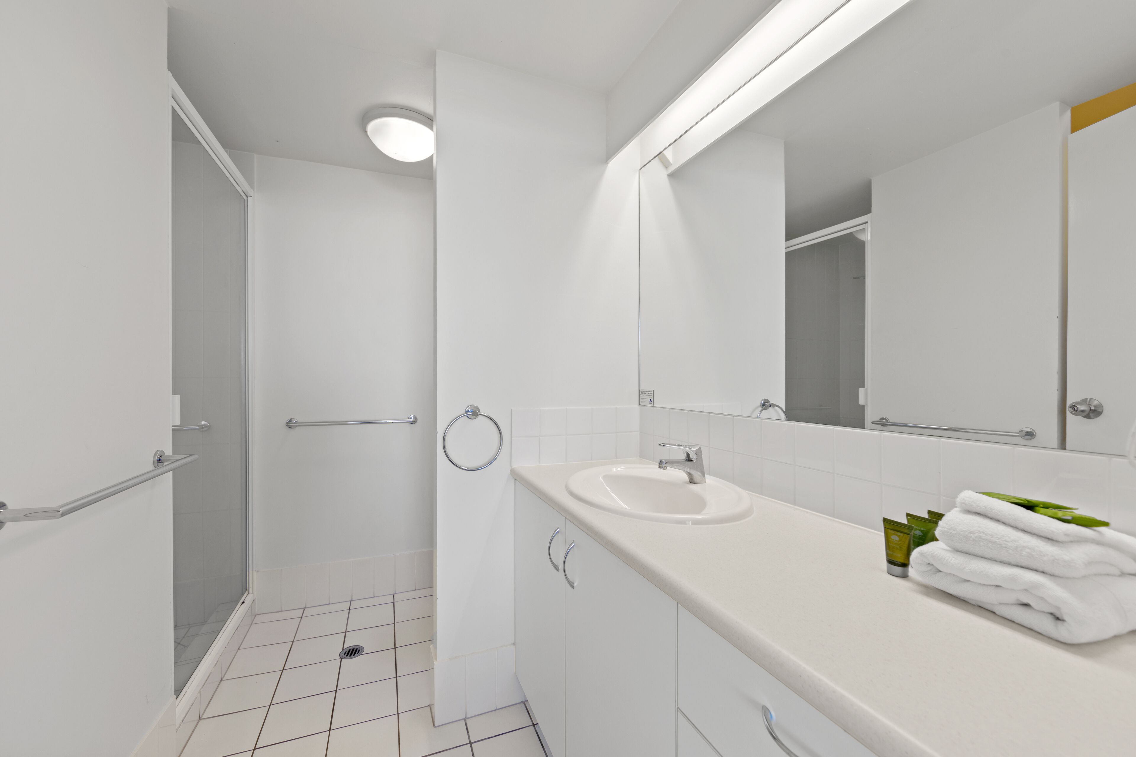 Une salle de bain moderne avec une douche en verre, des carreaux blancs, un lavabo et un miroir.