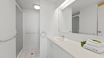 Une salle de bain moderne avec une douche en verre, des carreaux blancs, un lavabo et un miroir.