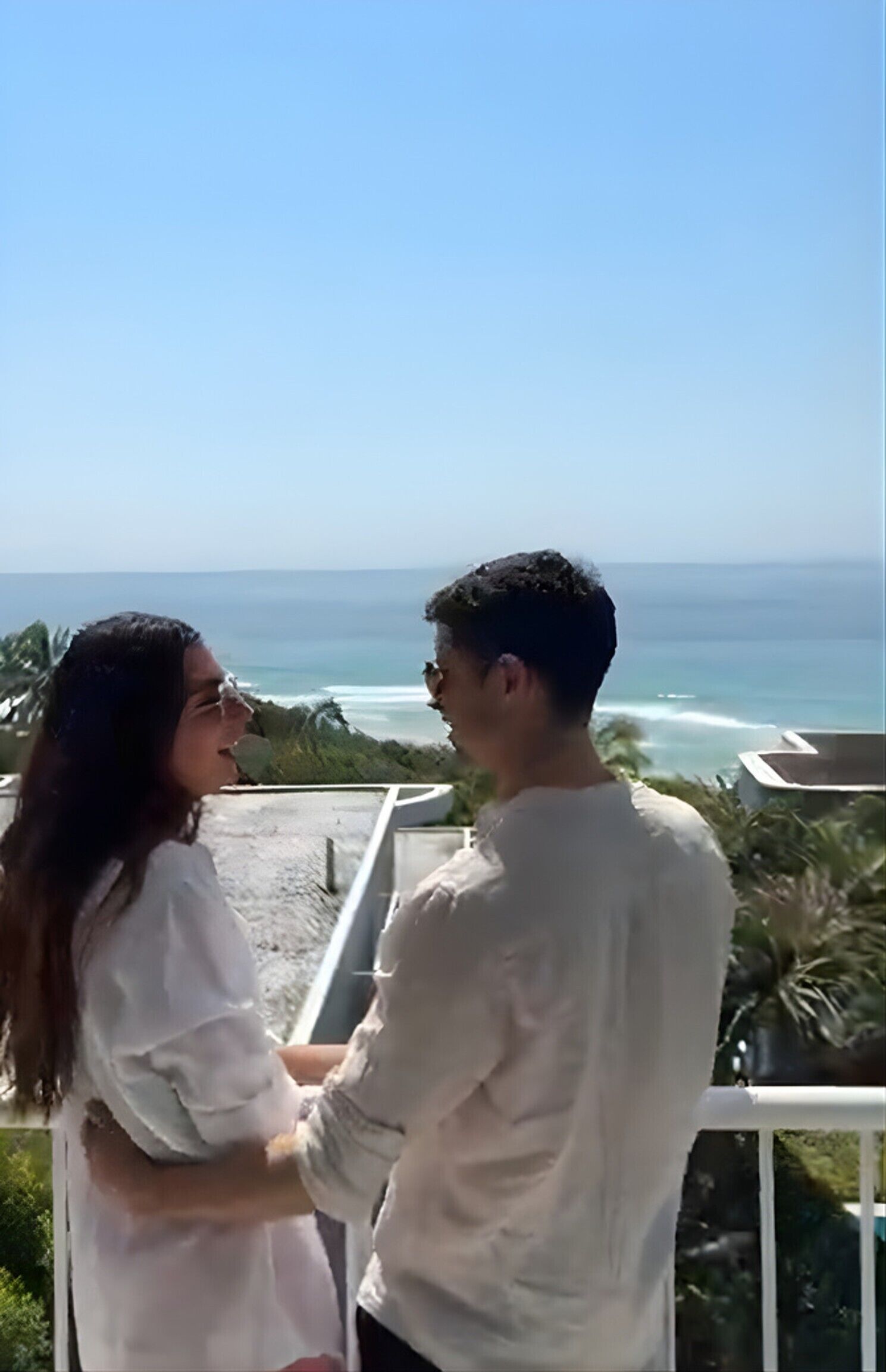 Dos personas en un balcón con vista al océano.