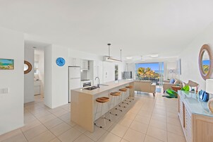 Una cocina moderna con una isla central, taburetes de bar y una zona de comedor con sofá y sillas.