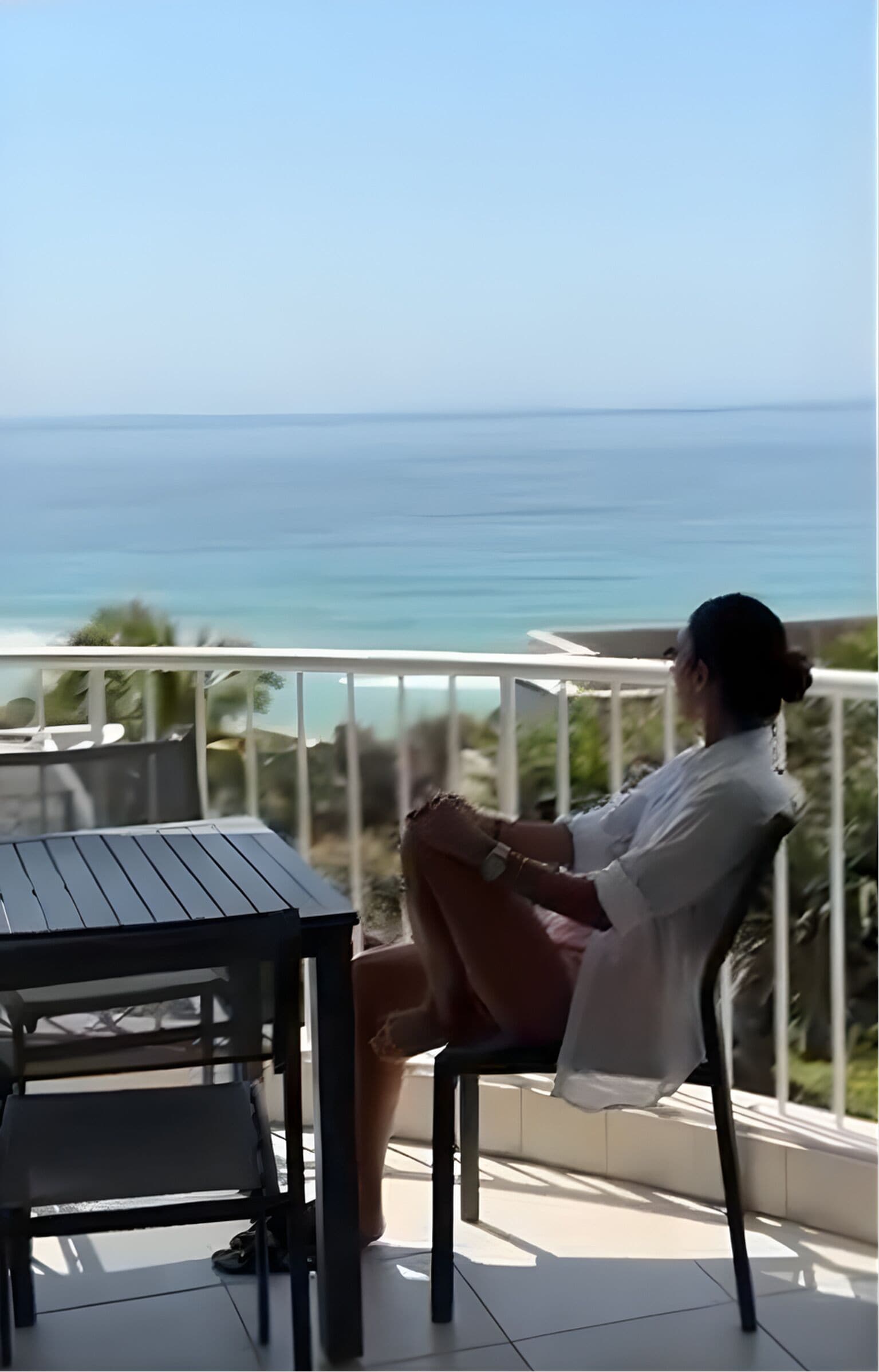 Una persona sentada en una silla en un balcón con vista a la playa.