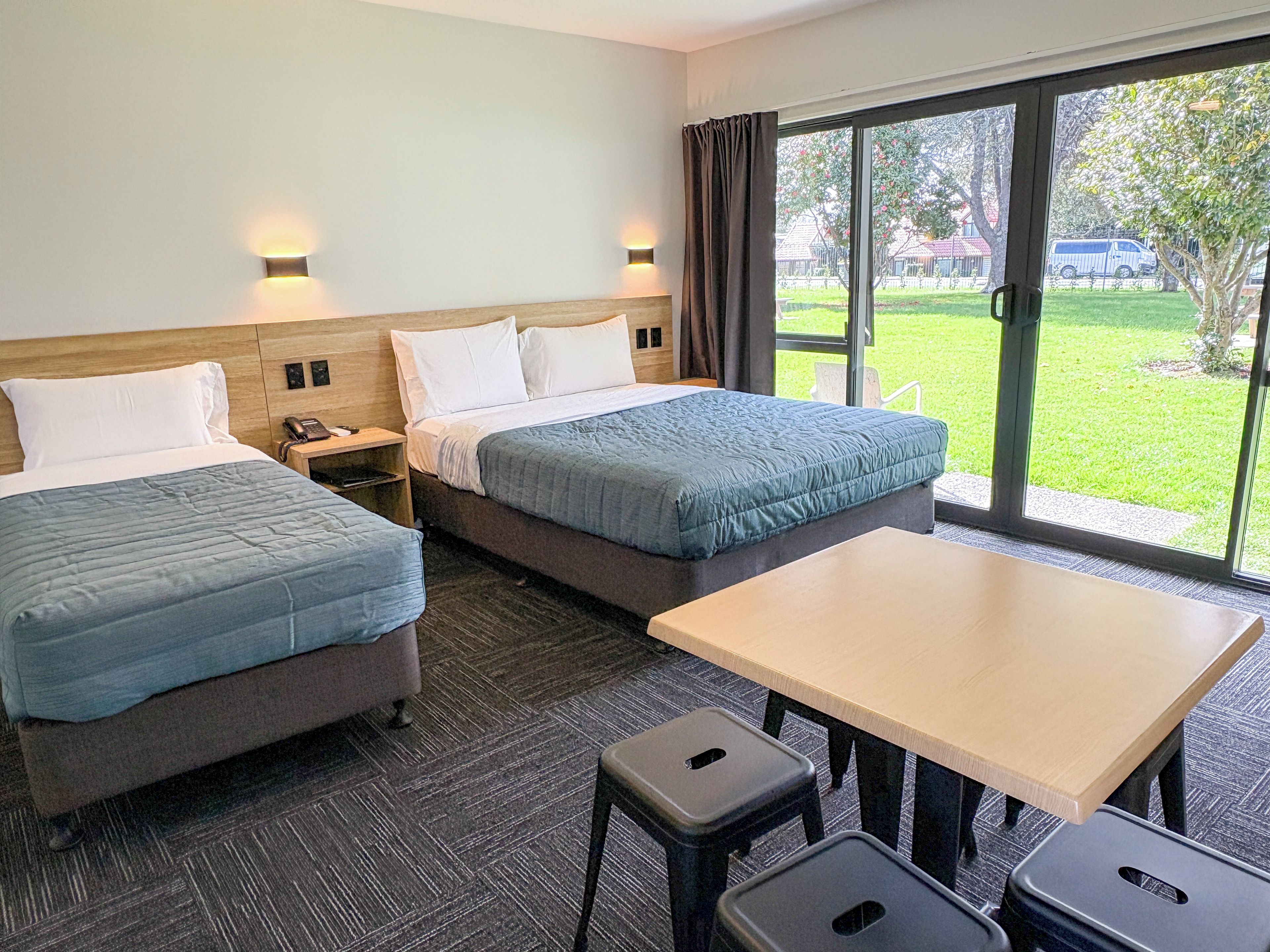 Ein Hotelzimmer mit zwei Betten, einem Schreibtisch und einem großen Fenster mit Blick ins Freie.