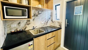 A kitchen with a black countertop, wooden cabinets, a microwave, and a sink. - Airport Gold Star Motel (Auckland)