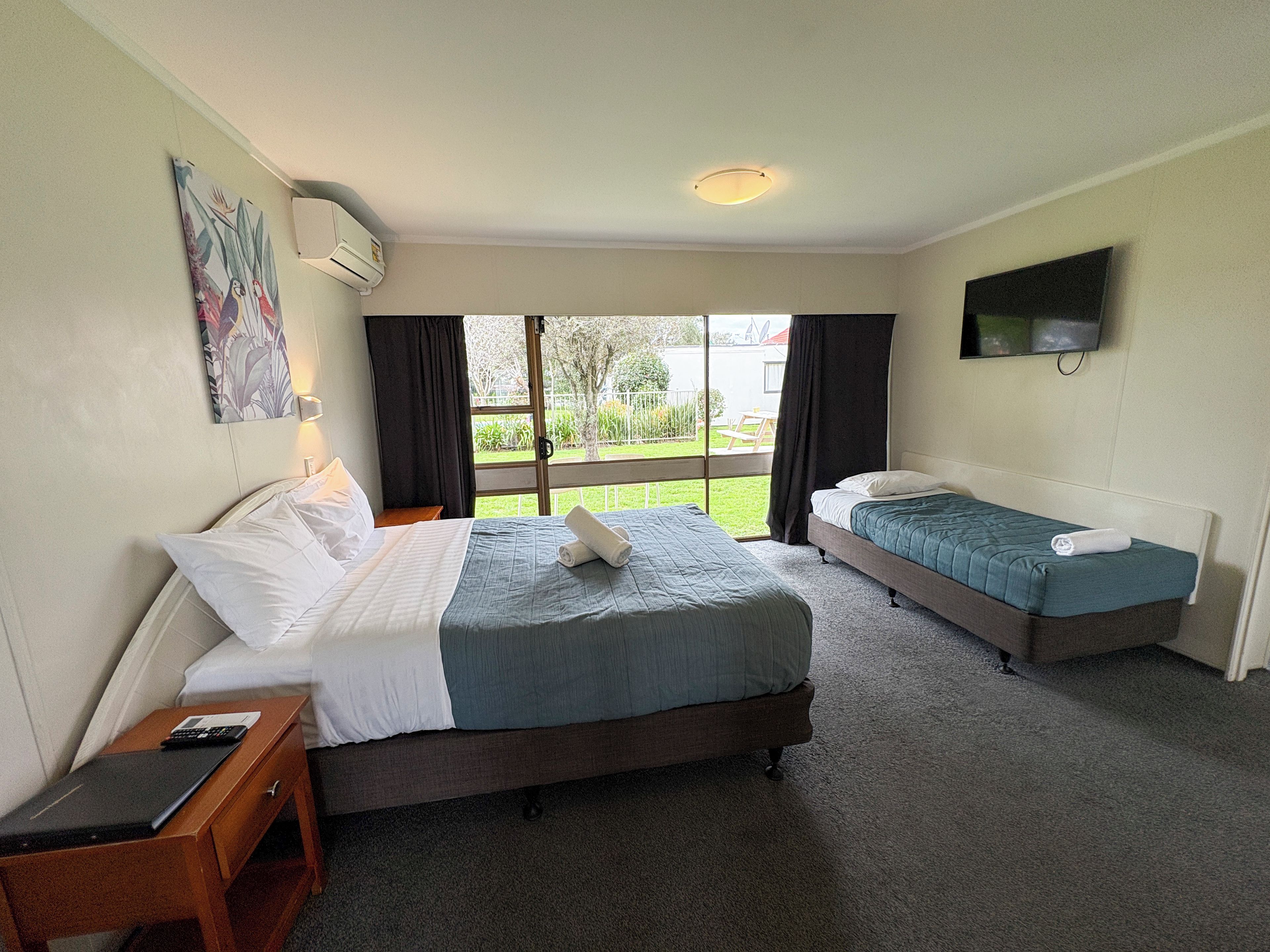 A hotel room with two beds, a desk, a TV, and a window with curtains.