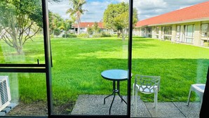 A room with a large window overlooking a grassy courtyard, a small table, and a chair. - Airport Gold Star Motel (Auckland)