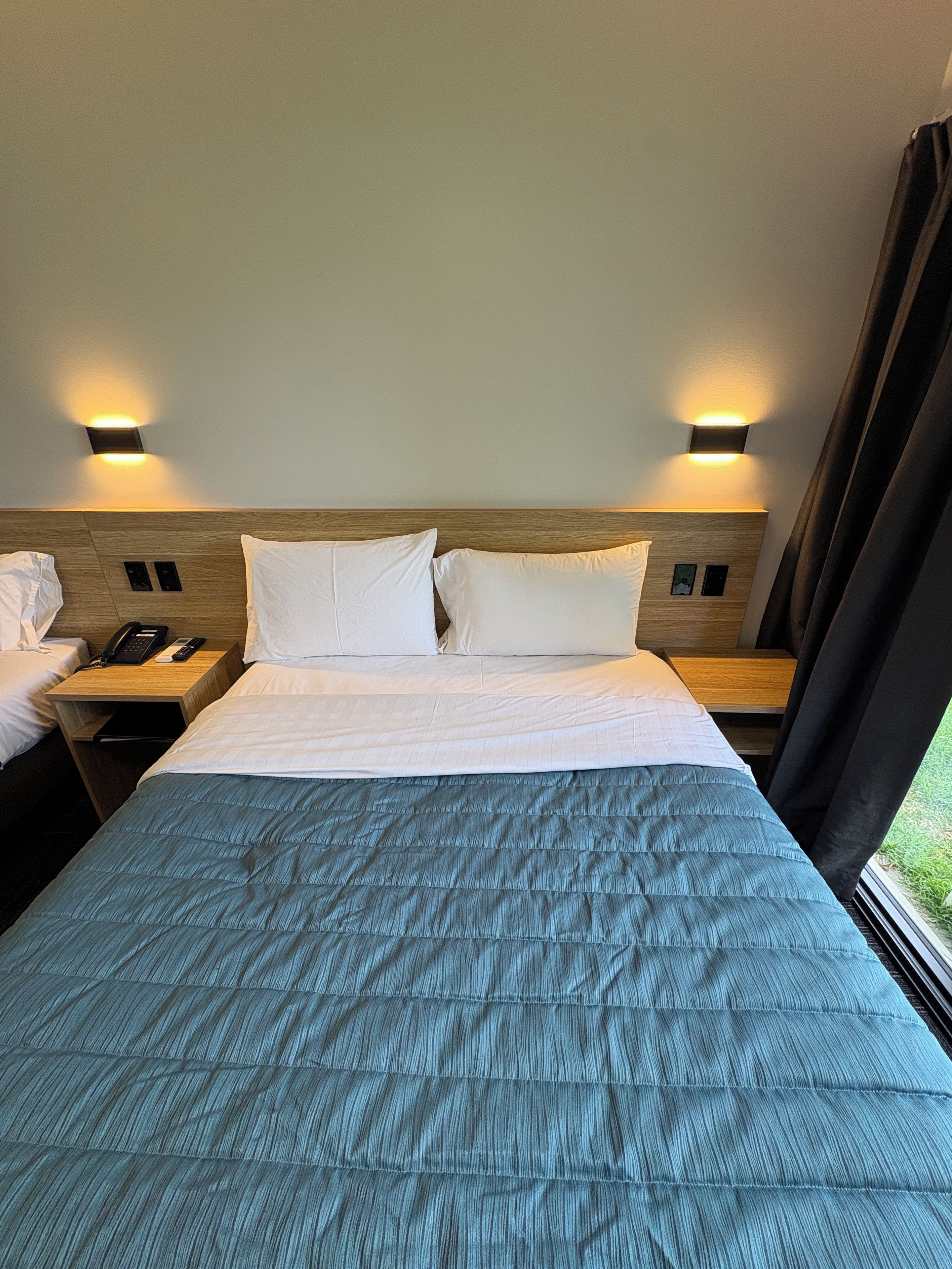 Een hotelkamer met een bed, nachtkastjes, een telefoon en een nachttafeltje.