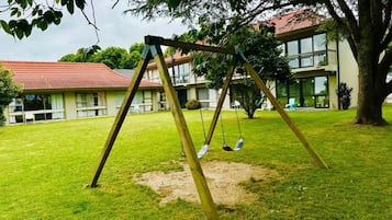 Baloiço numa área gramada, com um edifício ao fundo.