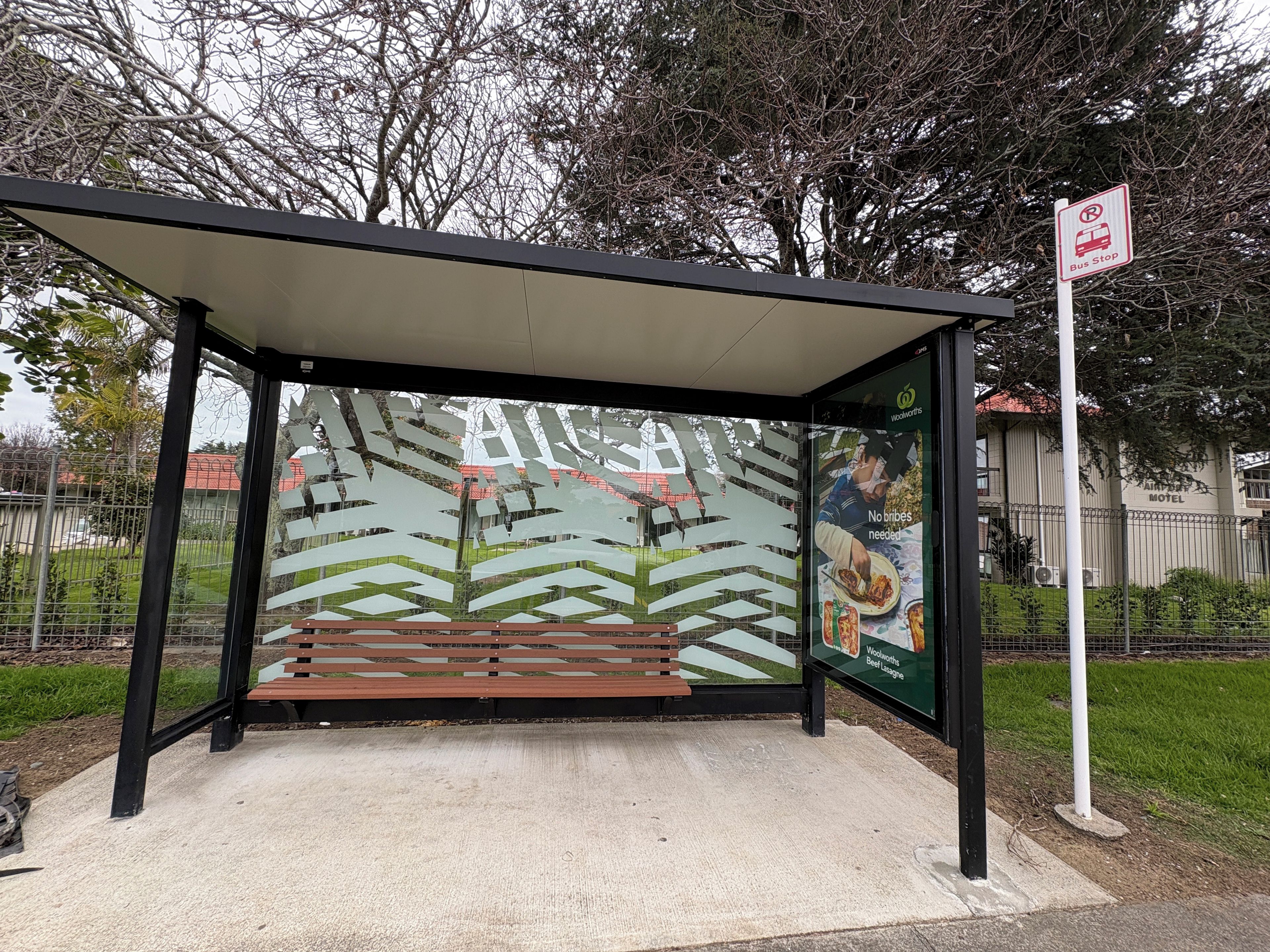A bus stop with a shelter, a sign indicating no bribes needed, and a nearby motel.