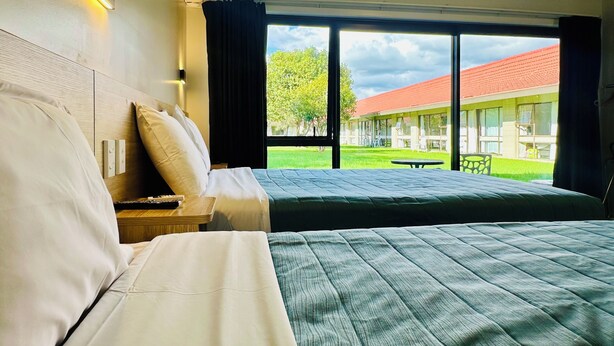 A hotel room with two beds, a large window, and a view of the building's exterior. - Airport Gold Star Motel (Auckland)