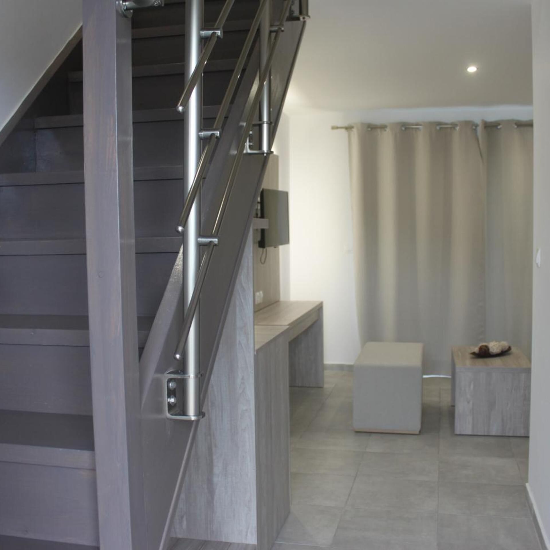 A modern staircase with metal railings, a bench, and a small table in a neutral-toned room with a tiled floor.