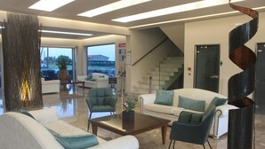A modern lobby with white sofas, a glass coffee table, and a staircase. - Vallian Village (Rhodes)