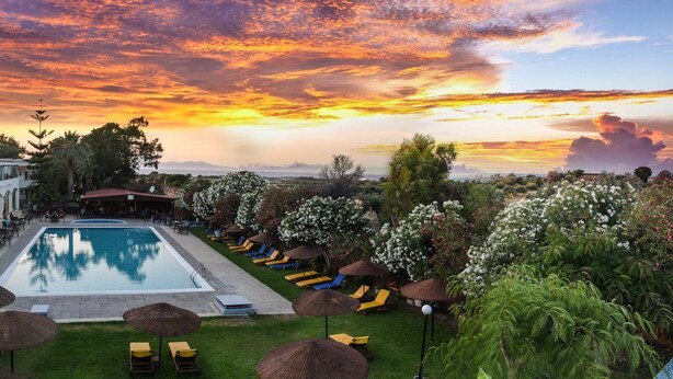A resort with a swimming pool, lounge chairs, and a view of the sunset. - Vallian Village (Rhodes)
