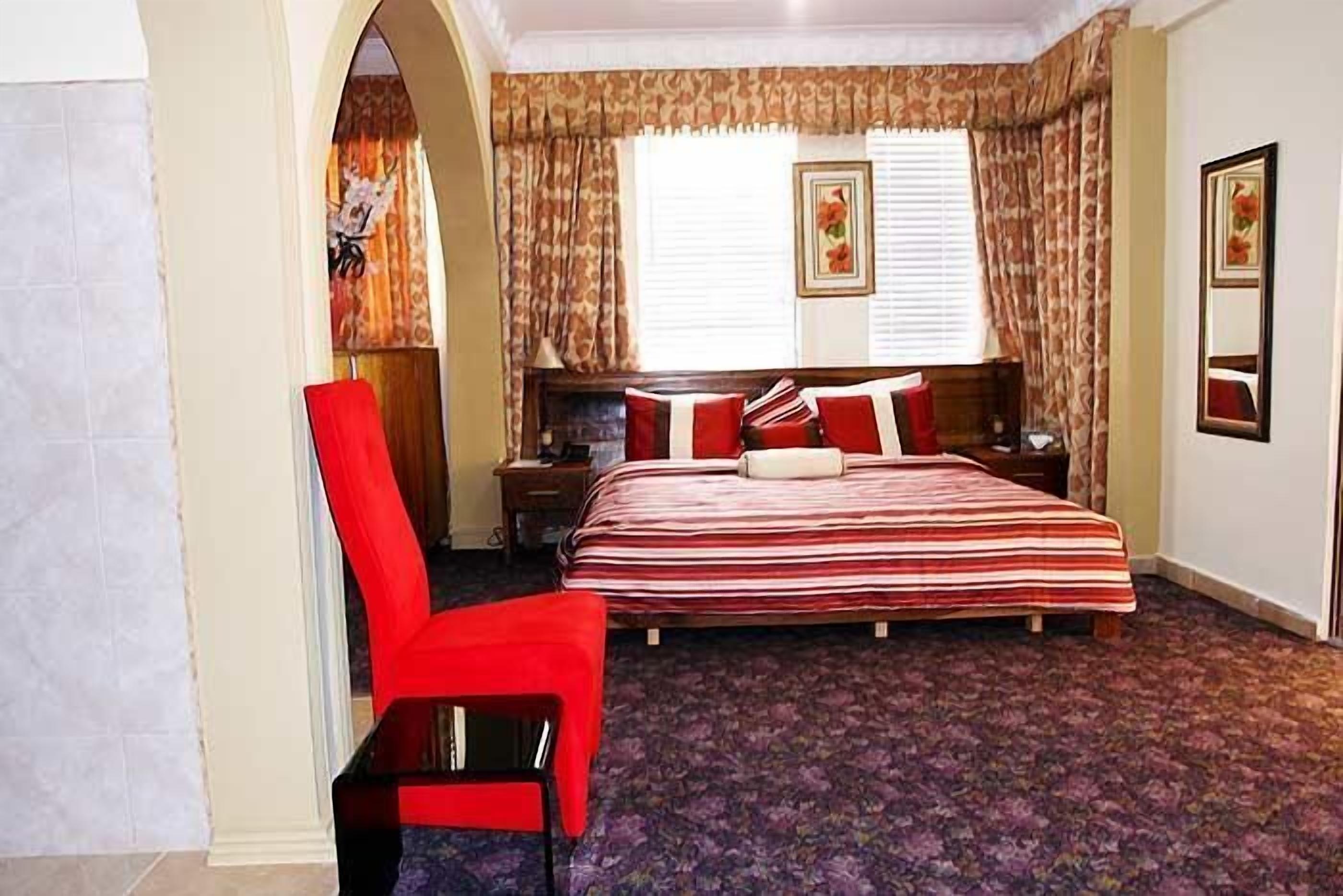 Une chambre à coucher avec un lit, une chaise, une table de chevet et une fenêtre avec des rideaux.