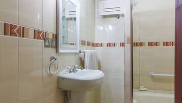 Un baño con lavamanos, espejo, toallero y zona de ducha.