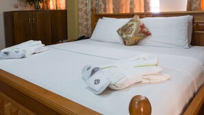 Una cama bien hecha con sábanas blancas, cabecera de madera y un cojín decorativo.