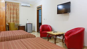 Une chambre d’hôtel avec deux lits, une télévision, un fauteuil rouge, une petite table et un meuble en bois.