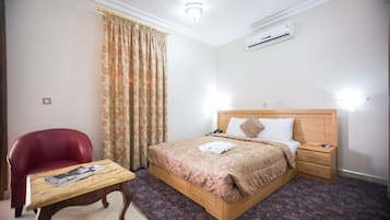 Una camera d'albergo ben ordinata con un letto in legno, una poltrona rossa, un piccolo tavolino e un tappeto decorato.