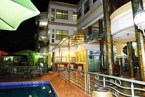 Zona de piscina con borde de baldosas, barandilla metálica y una sombrilla verde.