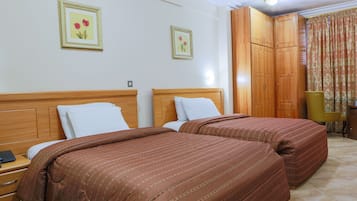 A hotel room with two beds, wooden headboards, a small desk with a telephone, and a chair.