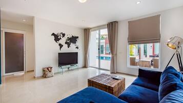 A modern living room with a large blue sofa, a wooden coffee table, a flat-screen TV, and a world map on the wall.