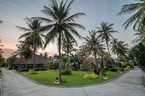 A tropical resort with palm trees, a thatched-roof building, and a well-maintained lawn. - The Beach Village Resort (Sam Roi Yot)