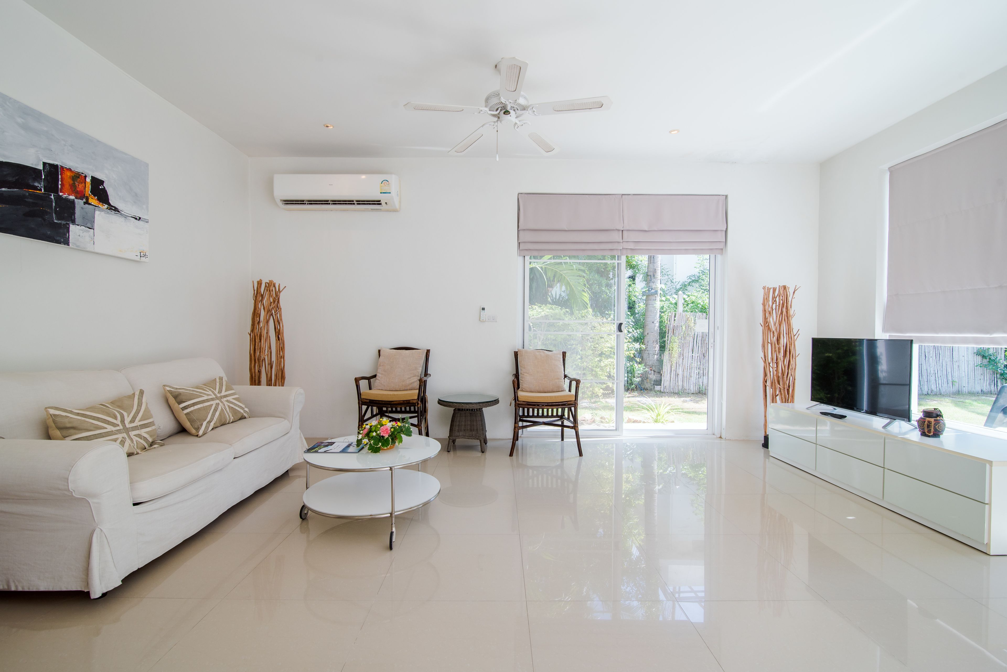 A modern living room with a white sofa, two armchairs, a coffee table, and a TV on a white cabinet.