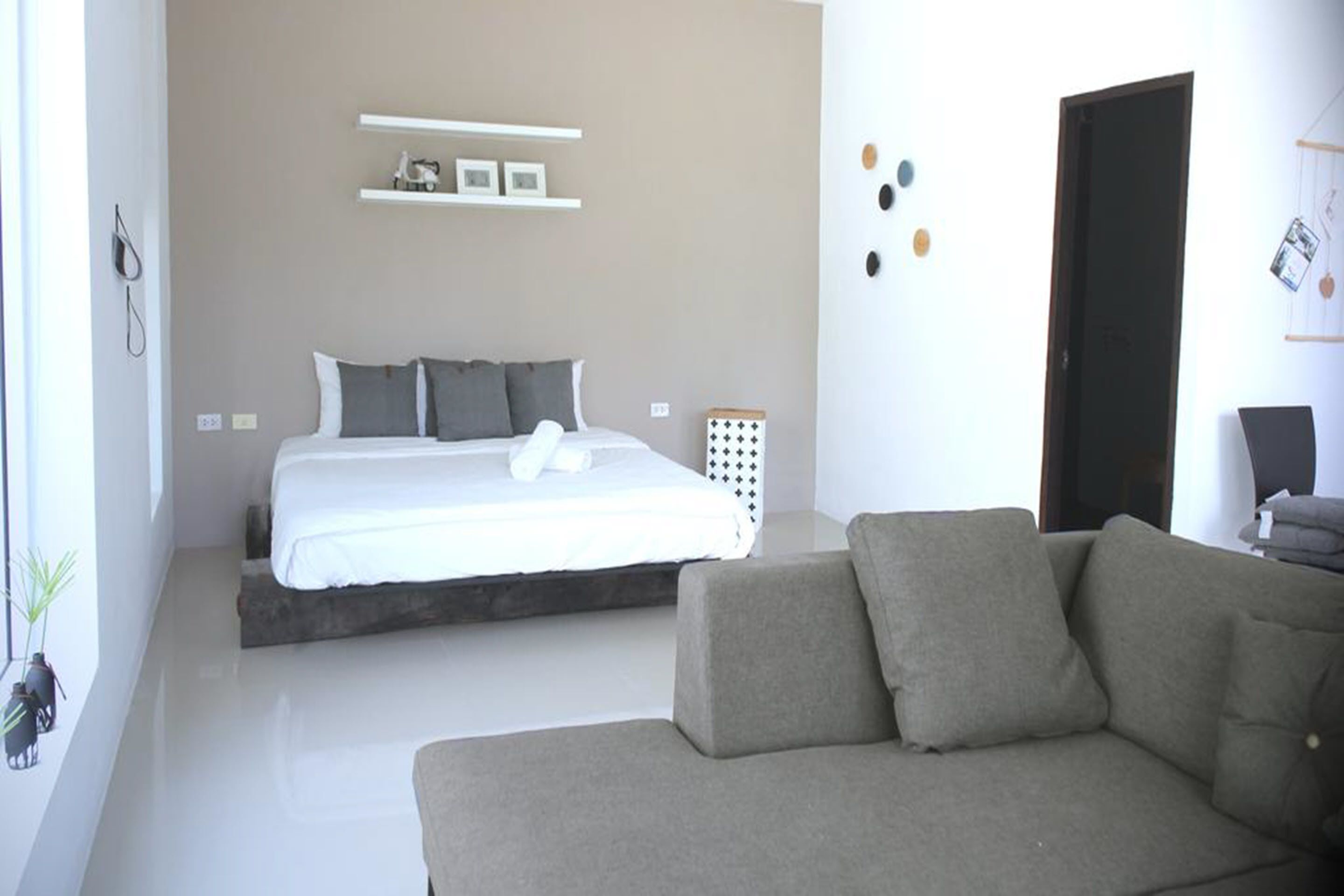 Un dormitorio moderno con una cama, un sofá gris y una estantería de pared con objetos decorativos.