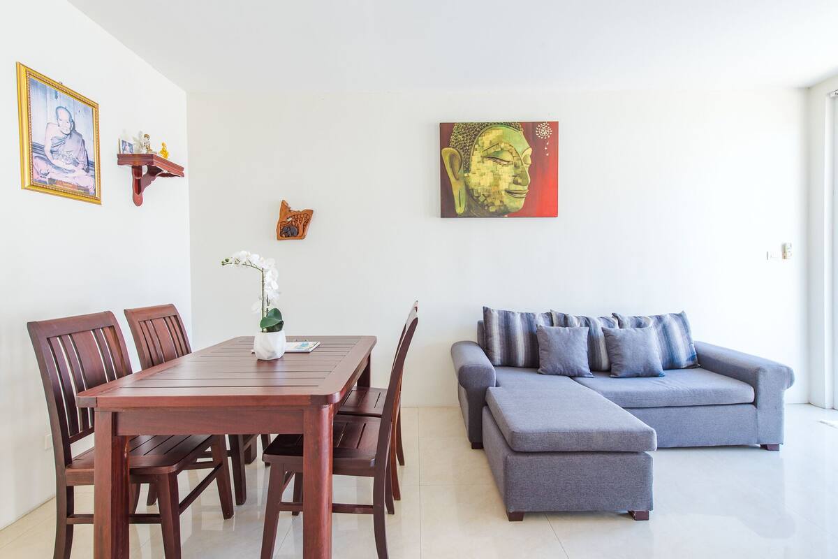 Un salon moderne avec une table à manger en bois, un canapé gris et des œuvres d’art accrochées aux murs.