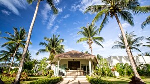 Un resort con una edificación de techo de paja, rodeado de palmeras y un jardín cuidado.