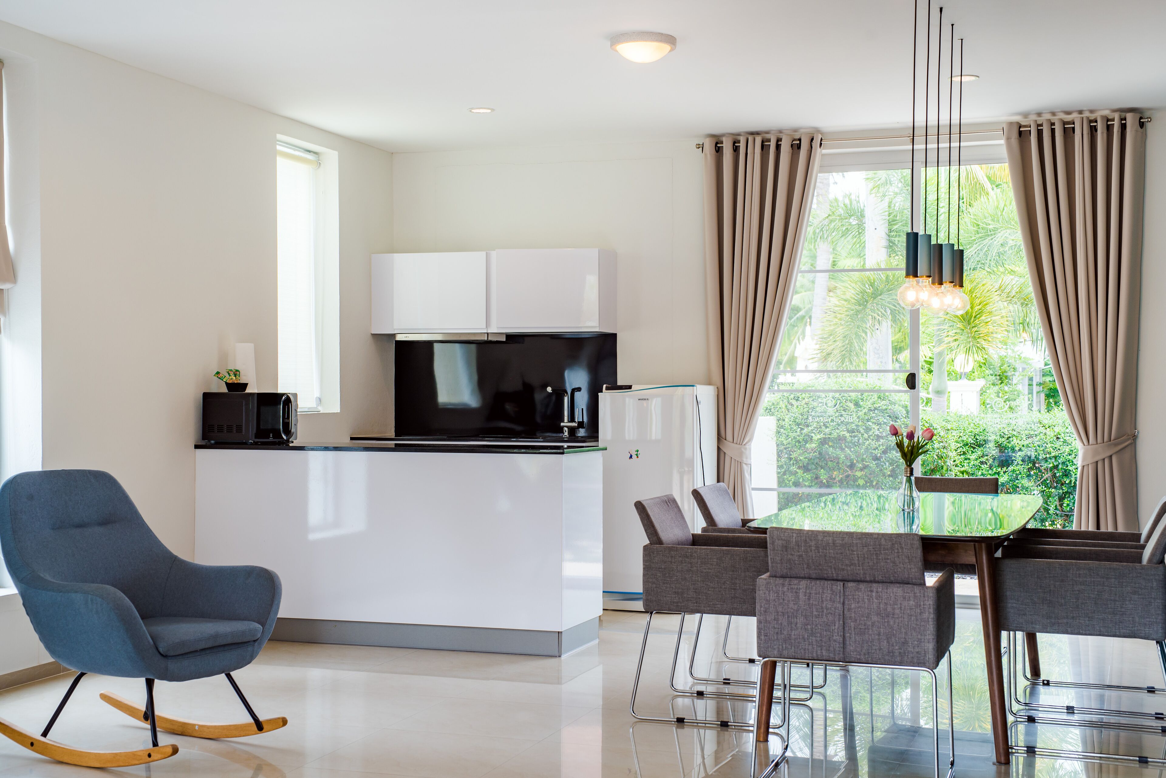 A modern kitchen with white cabinets, a black microwave, and a glass-top dining table with grey chairs.