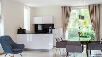 A modern kitchen with white cabinets, a black microwave, and a glass-top dining table with grey chairs.