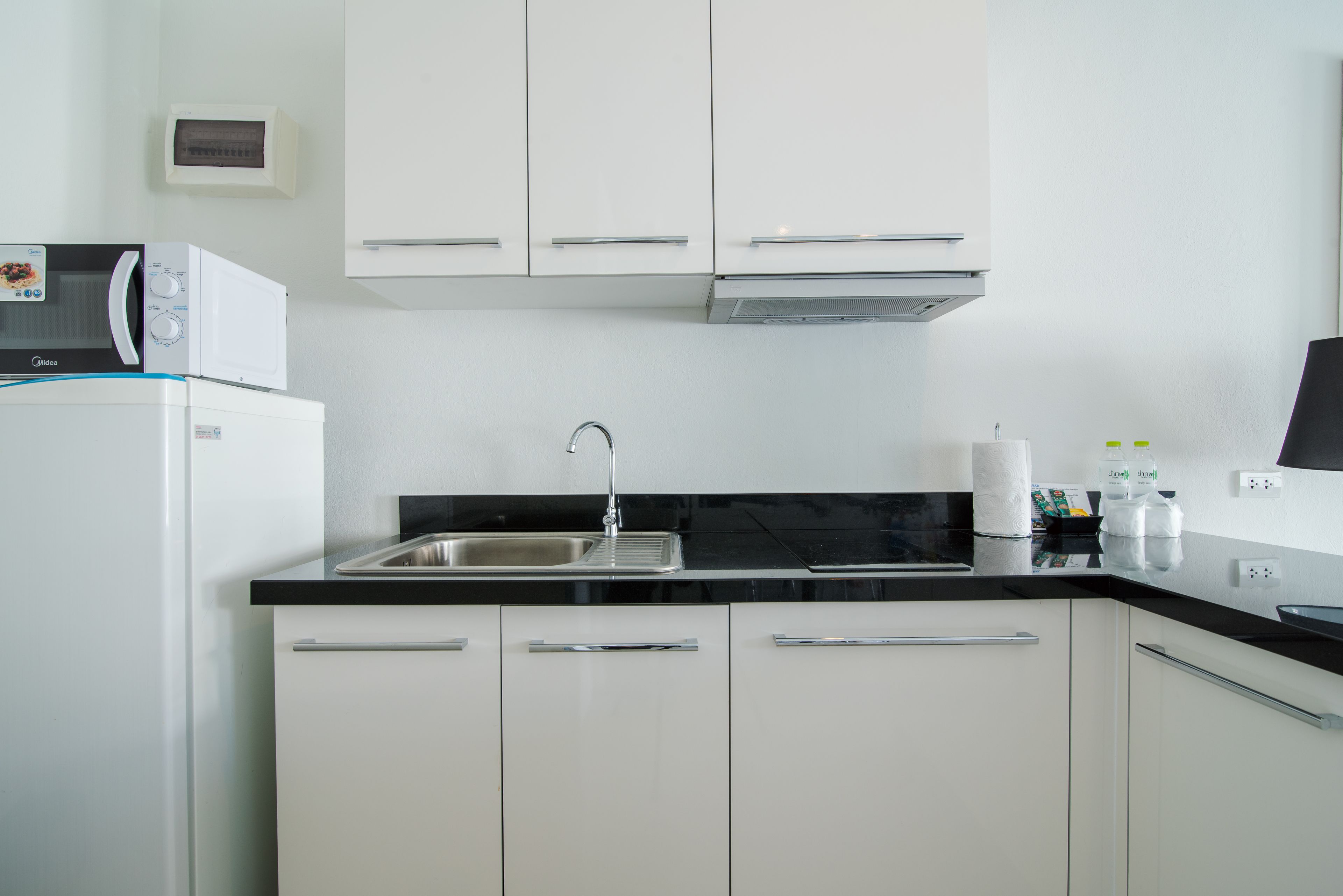 Una cocina moderna con armarios blancos, encimera negra, microondas integrado y pileta de acero inoxidable.