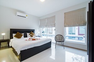 Habitación de hotel moderna con una cama grande, una silla y vistas de la ciudad a través de amplios ventanales.