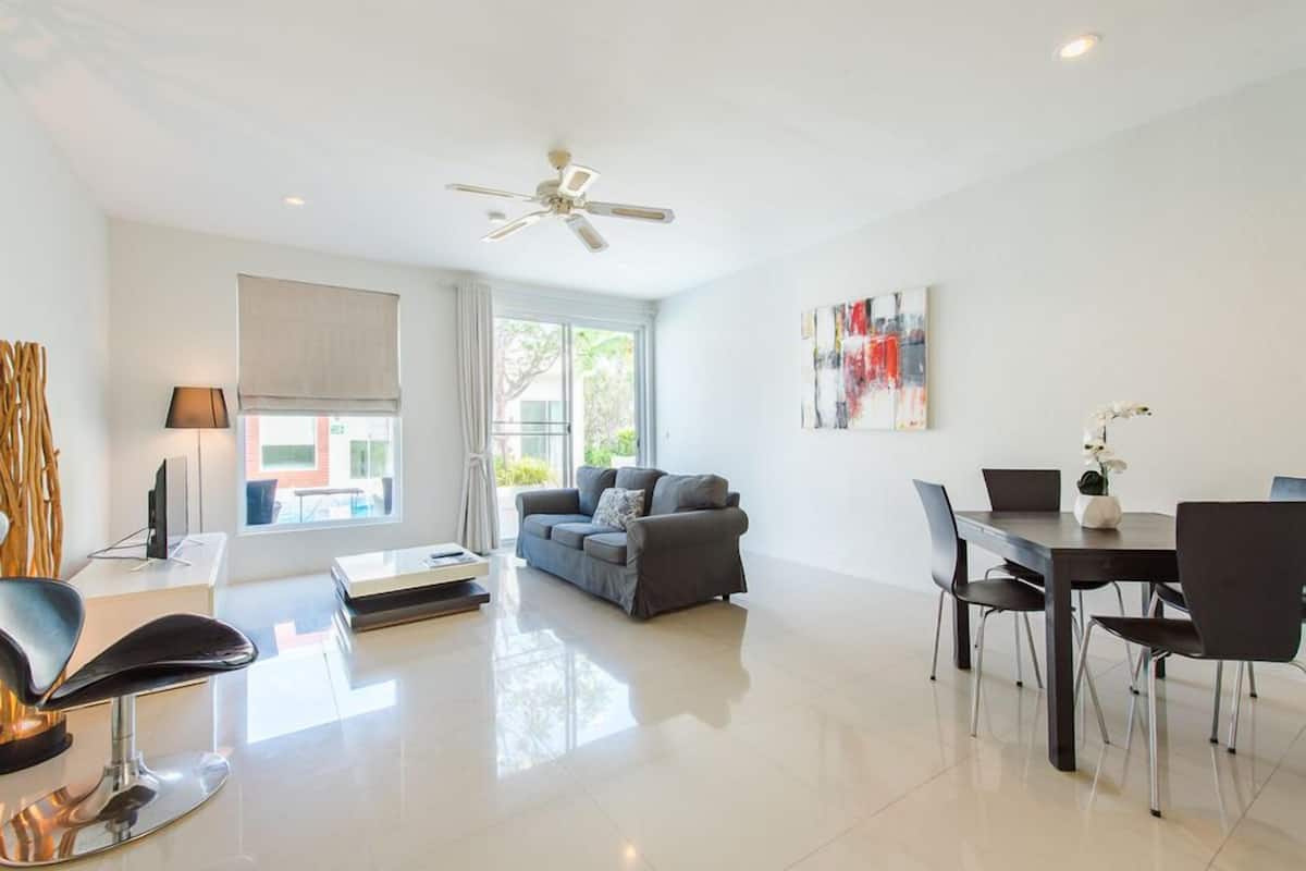 Un salon moderne avec un canapé gris, une table à manger avec des chaises, un ventilateur de plafond et une grande fenêtre avec des rideaux.