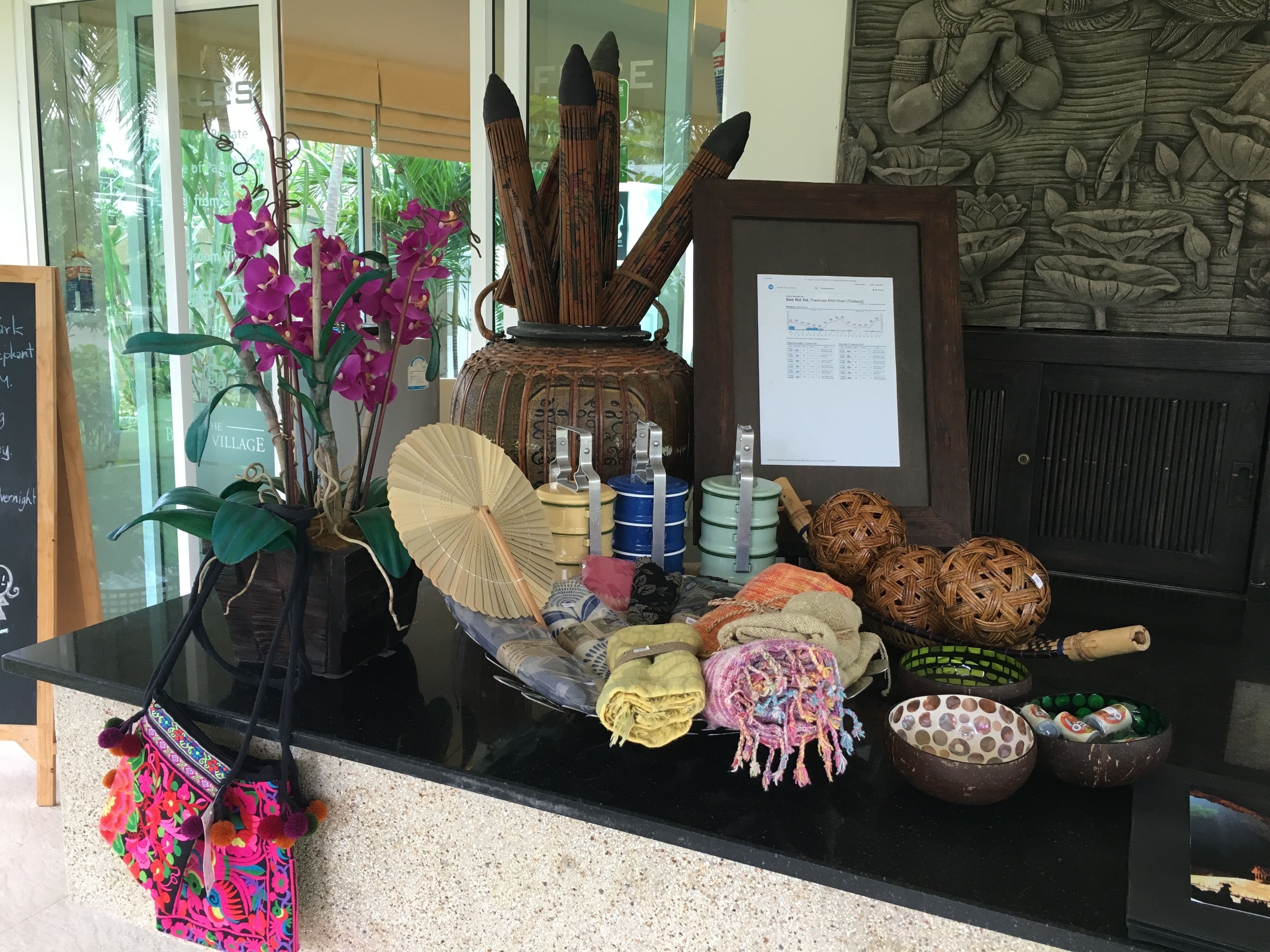 A reception desk with a vase of purple orchids, a fan, and various decorative items including woven baskets and a framed picture.