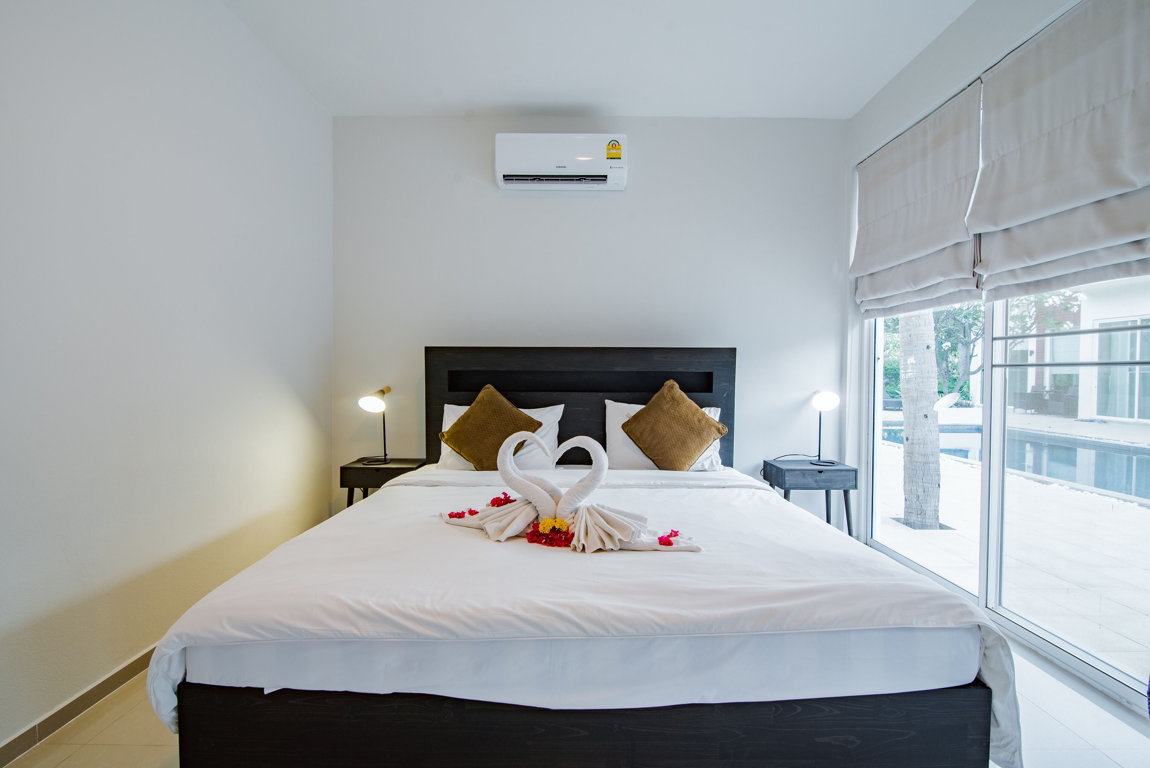 Una habitación de hotel con una cama bien hecha, un aire acondicionado de pared, una lámpara de noche y una ventana con vistas al exterior.