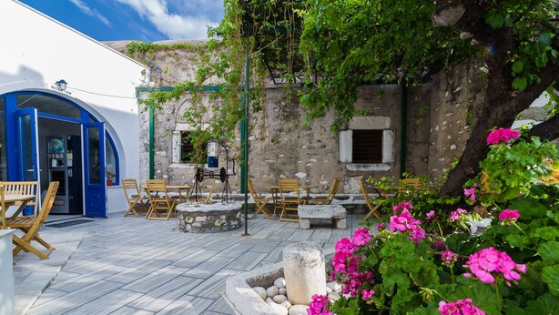 Un espacio al aire libre con mesas y sillas de piedra, una entrada azul y una pared de piedra con plantas.