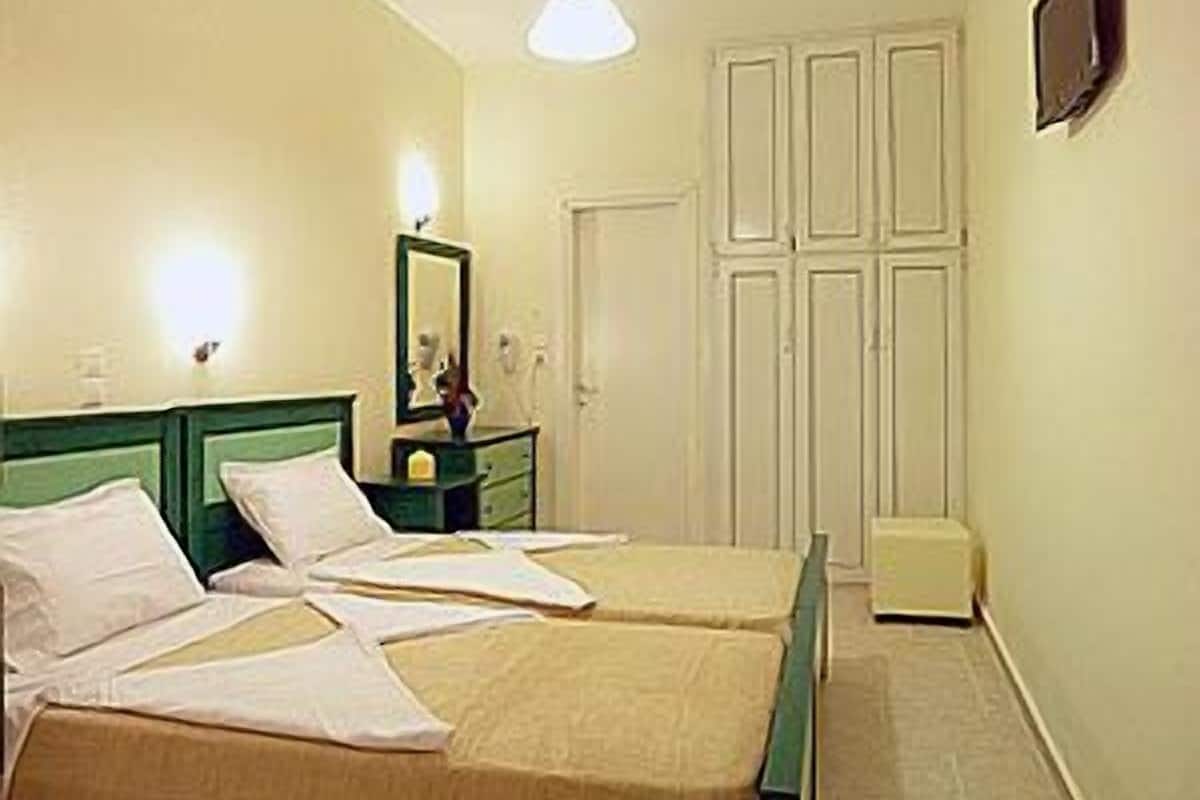 A room with two single beds, a nightstand, a mirror, a wardrobe, and a television on the wall.
