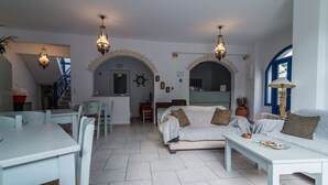 Amplia sala de estar con sofá, mesa de comedor y sillas. Dos puertas arqueadas conducen a otras habitaciones.