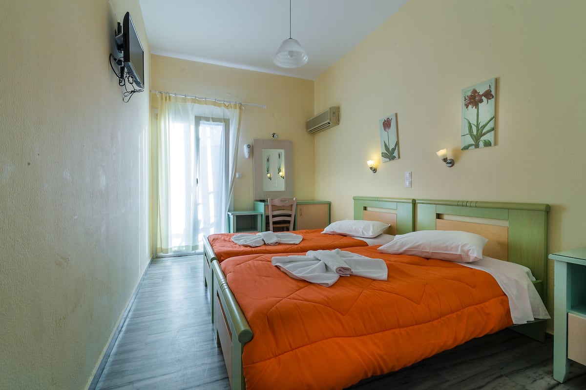 A hotel room with two beds, a TV, a mirror, and a window with curtains.