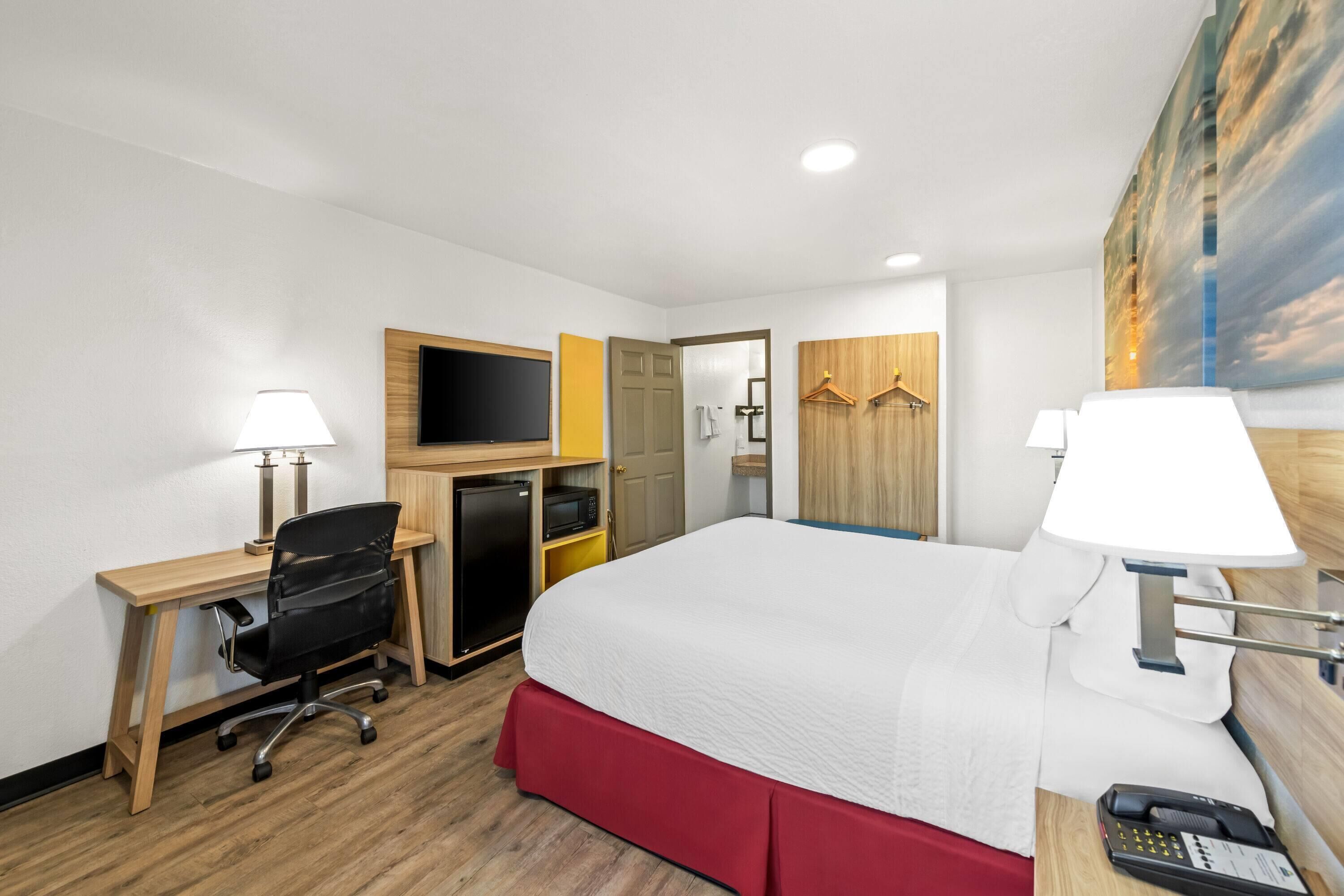 Habitación de hotel con cama, escritorio, silla, televisión, microondas y un cuadro en la pared.